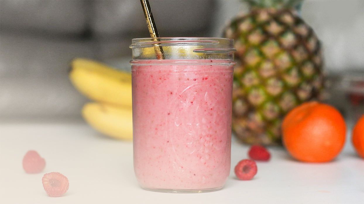 Himbeershake Glas Metallstrohhalm weisse Arbeitsplatte ganze Ananas Himbeeren Bananen